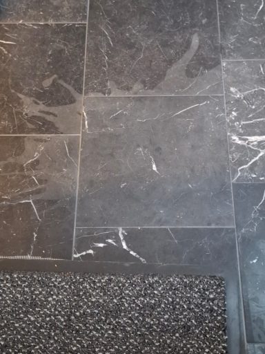 Matt gewordener Nero Marquina Marmor mit Flecken und Verätzungen im Eingangsbereich.
